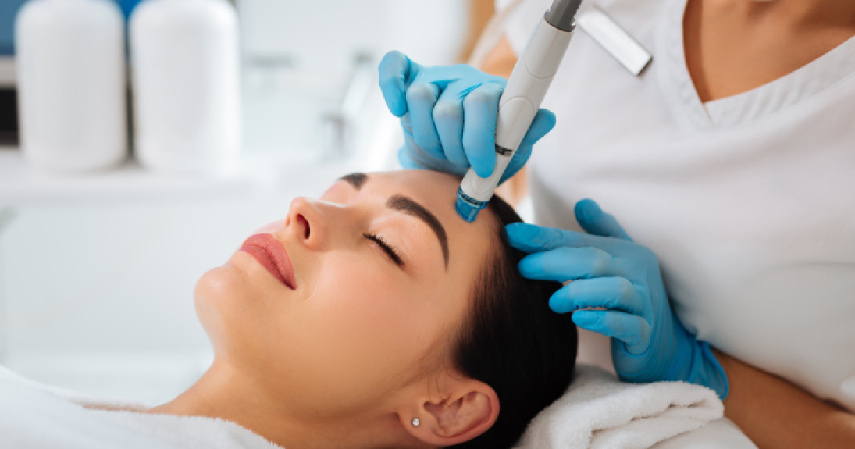 A woman receiving a HydraFacial treatment from a skincare professional wearing blue gloves in Evans, GA